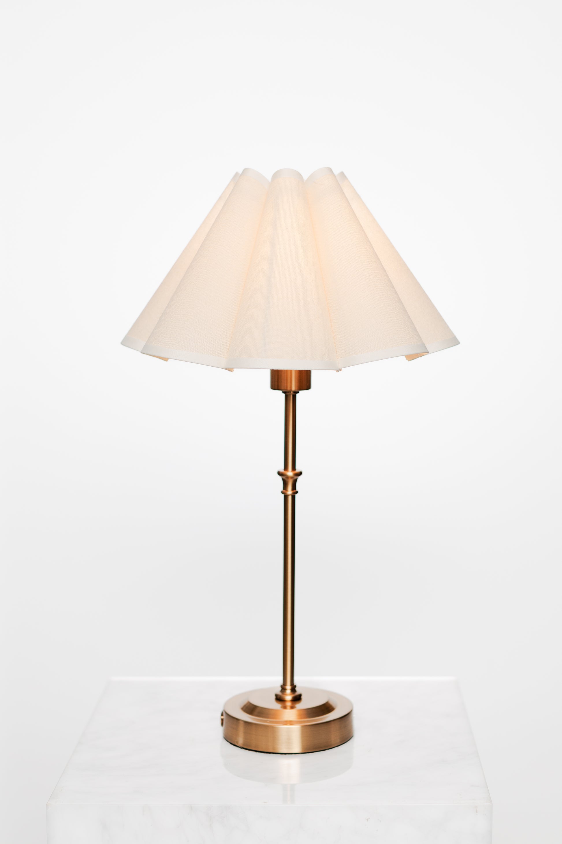 Neutral nook with brass lamp and textured cushion by window.